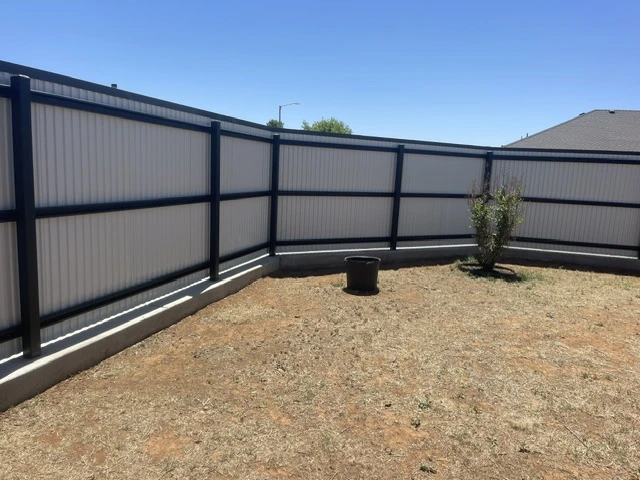 Black metal fence with white vertical ribbed panels installed on a concrete footing enclosing a residential backyard.