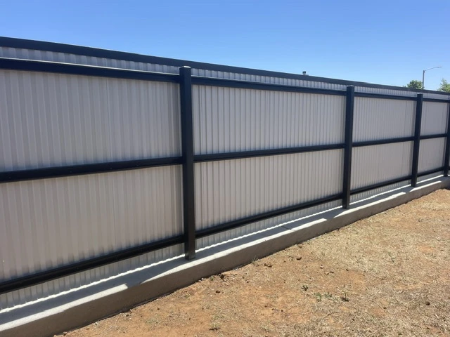 Custom black steel fence with white ribbed metal panels installed on a continuous concrete curb by a professional fencing contractor in Texas.