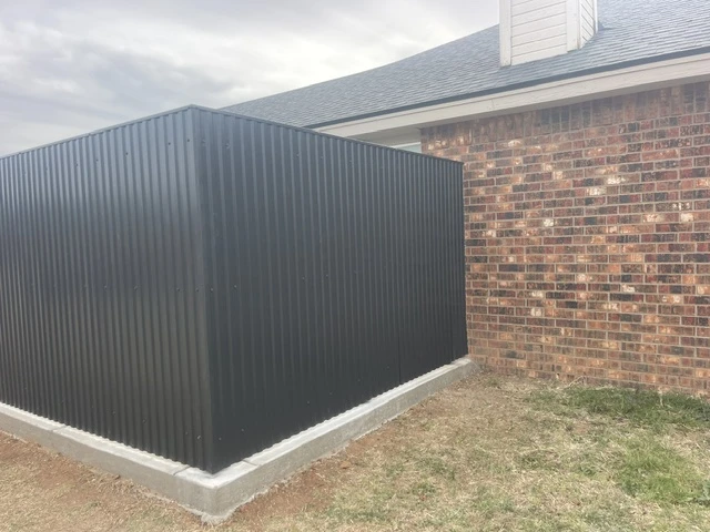Modern black welded steel privacy fence with vertical ribbed panels, built on a continuous concrete footing for durability and full privacy alongside a brick home