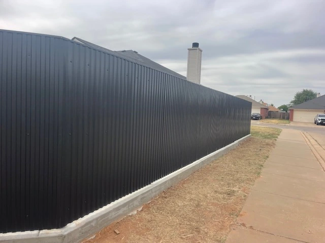 Long run of black welded steel privacy fencing with vertical ribbed metal panels, built on a solid concrete footing for maximum durability and full privacy along a residential property line.