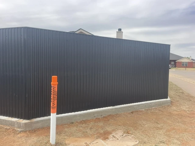 Modern black welded steel privacy fence with vertical ribbed panels, built on a continuous concrete footing for durability and full privacy along a residential corner lot.