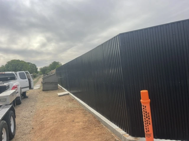 Long run of black welded steel privacy fencing with vertical ribbed metal panels, built on a continuous concrete footing for enhanced durability and security at a Texas property.
