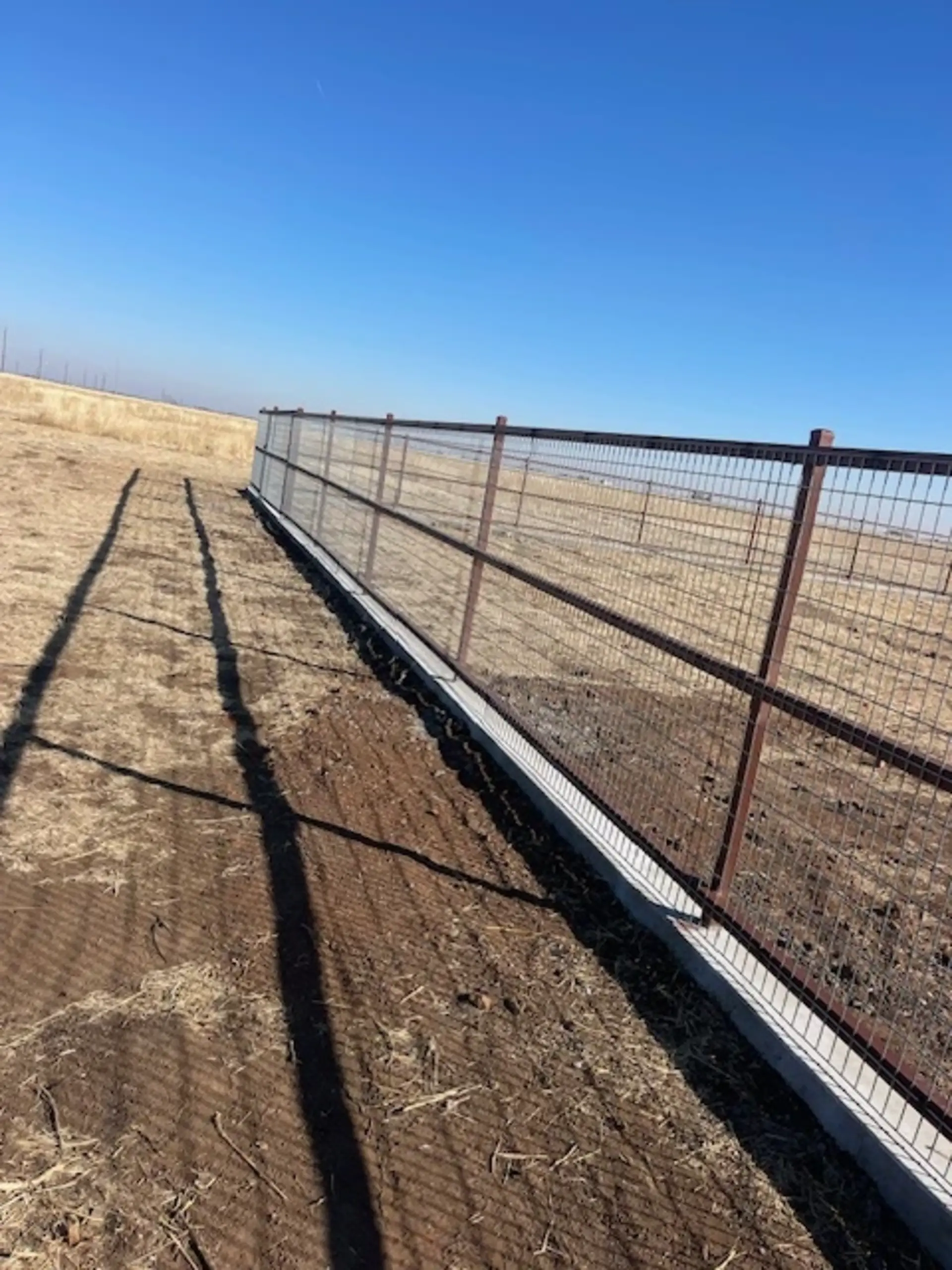 Ranch-rail style welded wire fencing with steel posts and concrete base in rural Lubbock Texas