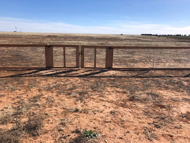 Custom double swing gate built into a 4-foot wood ranch rail fence with welded wire mesh for vehicle access, farm entry, and acreage fencing solutions